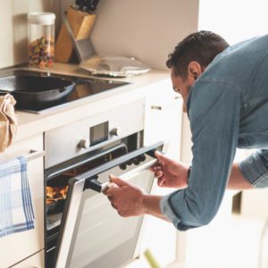 Man opening oven to check on food cooking inside.