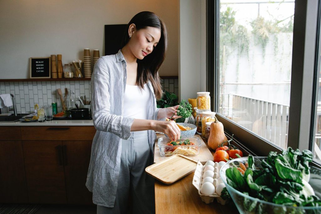 A woman is cooking a healthy meal using fresh ingredients like veggies and protein in her kitchen. 